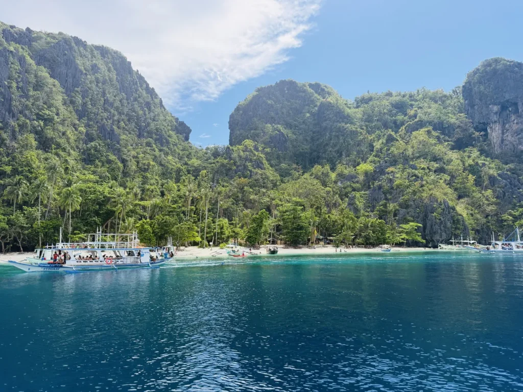 Barcas tradicionales en una bahía de agua turquesa al pie de acantilados de roca caliza en El Nido