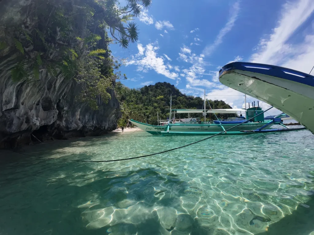 Proa de una barca sobre agua turquesa frente a una isla de roca caliza en El Nido