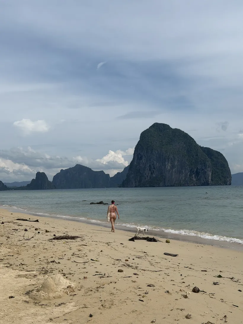 Cristina caminando por una playa de arena con islotes de piedra caliza al fondo