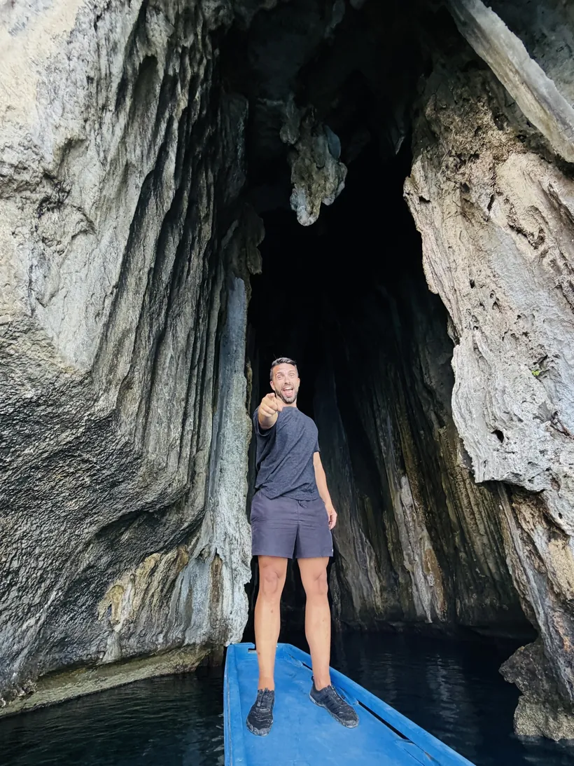 Juan de pie en la proa azul de una bangka a la entrada de una cueva de roca