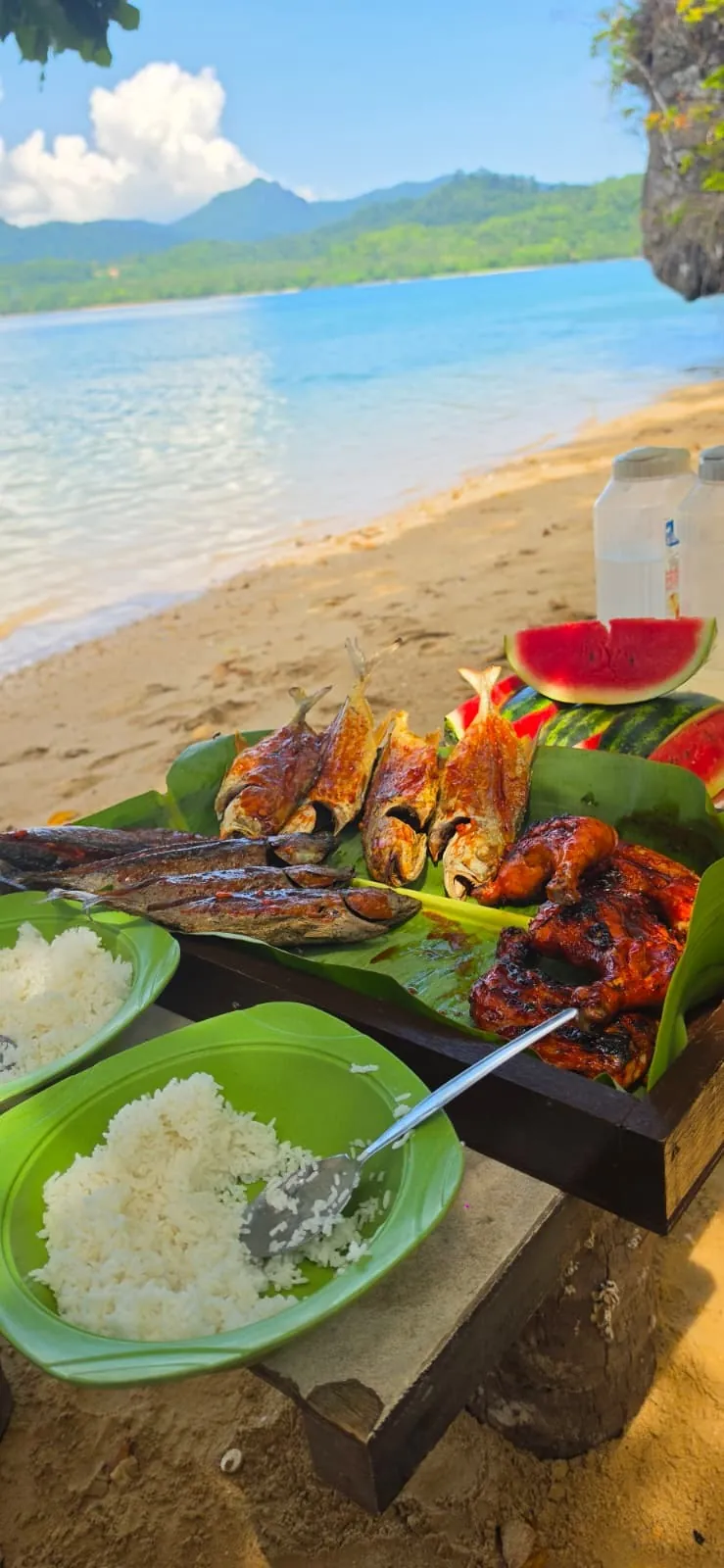 Pescado y pollo a la brasa sobre hojas de plátano, con arroz y sandía, en una playa