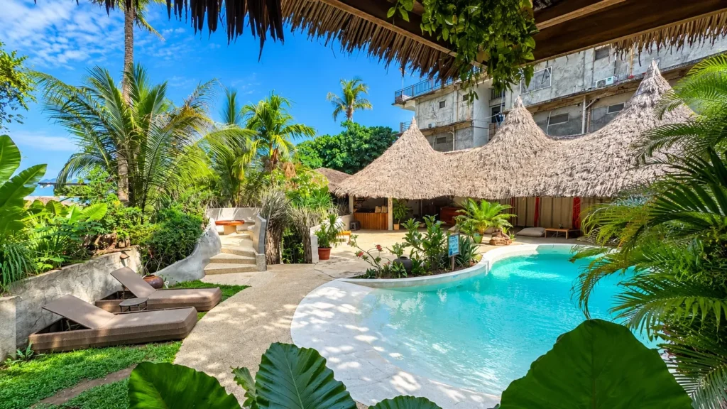 Piscina de formas curvas entre palmeras y cabañas con techo de paja en el Happiness Boutique Resort