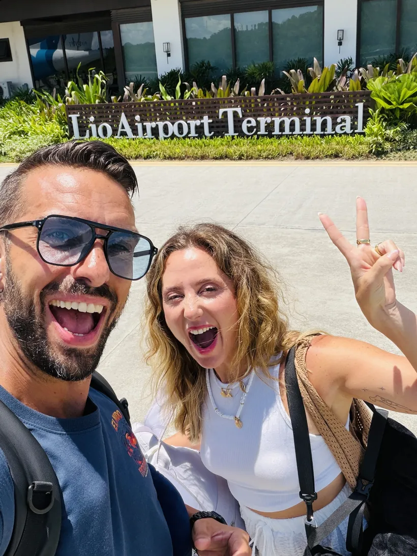 Cristina y Juan sonrientes delante del cartel de Lio Airport Terminal