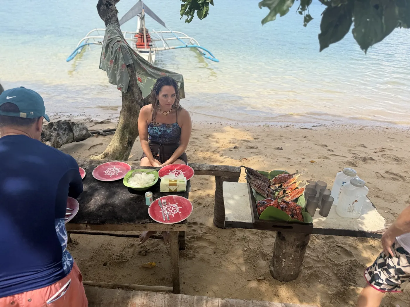 Mesa sencilla en la arena con platos, fruta y comida servida junto a la embarcación